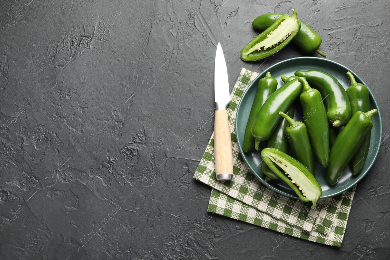 Photo of Fresh jalapeno peppers and knife on black textured table, flat lay. Space for text