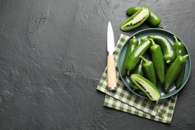 Photo of Fresh jalapeno peppers and knife on black textured table, flat lay. Space for text