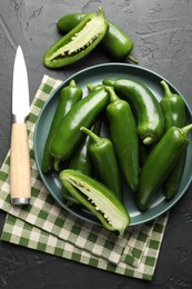 Photo of Fresh jalapeno peppers and knife on black textured table, flat lay