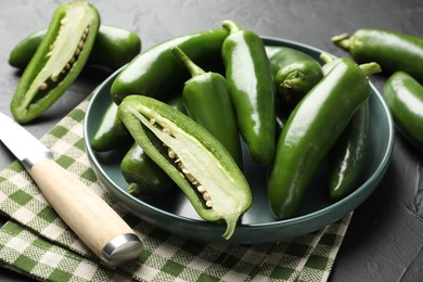 Photo of Fresh jalapeno peppers and knife on black table, closeup