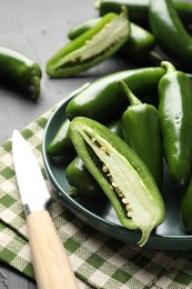 Photo of Fresh jalapeno peppers and knife on black table, closeup