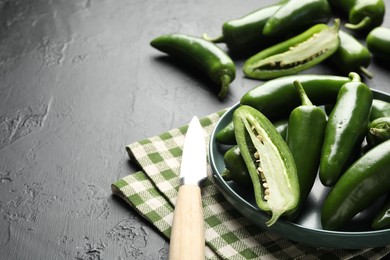 Photo of Fresh jalapeno peppers and knife on black textured table, closeup. Space for text