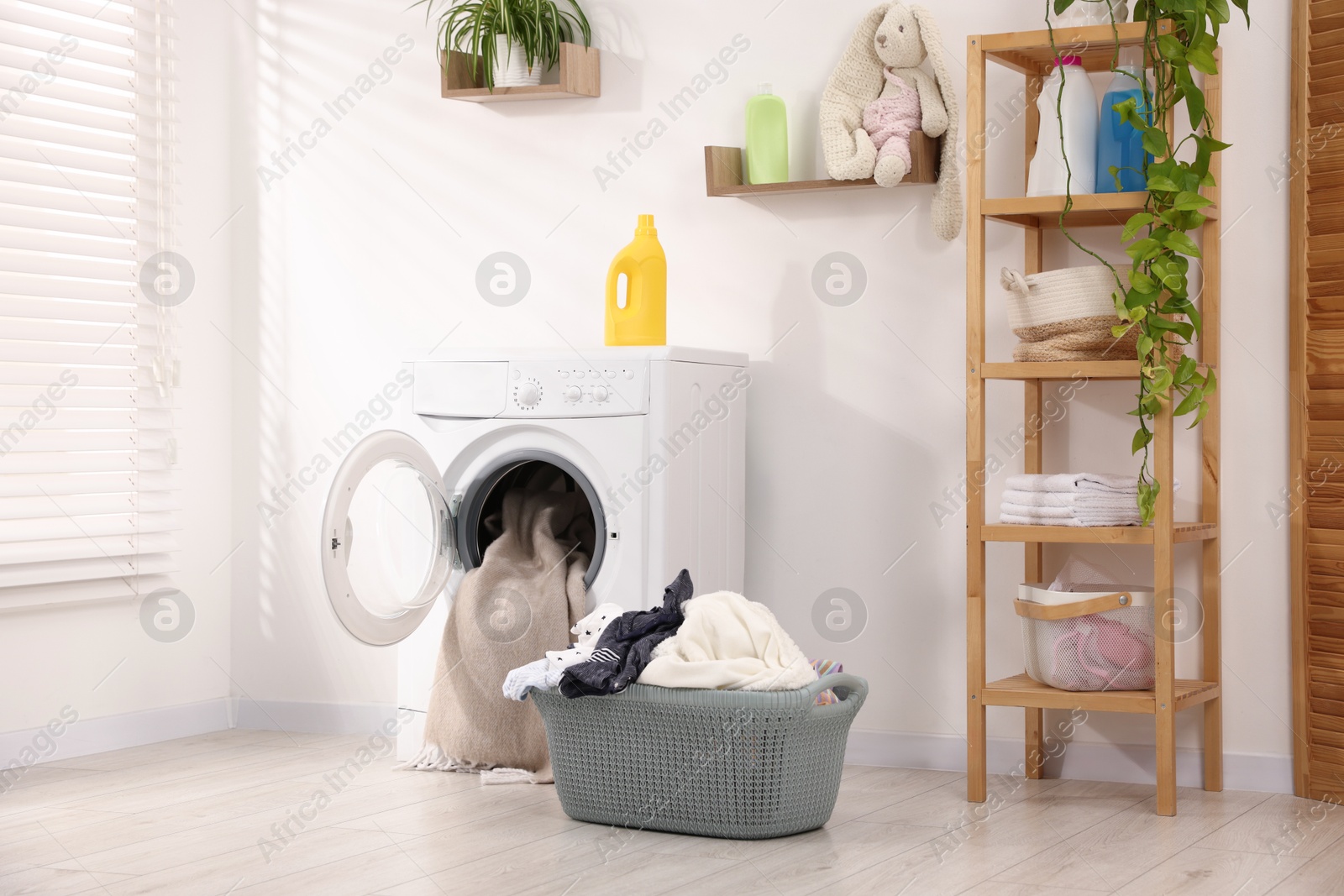 Photo of Washing machine with open door, detergent and laundry near white wall indoors