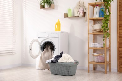 Photo of Washing machine with open door, detergent and laundry near white wall indoors