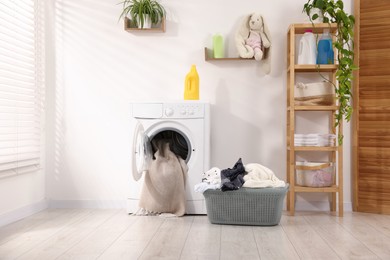 Photo of Washing machine with open door, detergent and laundry near white wall indoors