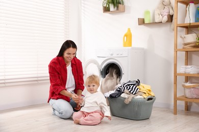 Photo of Smiling housewife with her baby doing laundry at home
