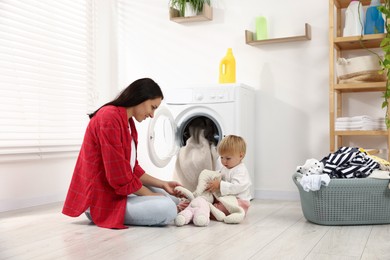 Photo of Smiling housewife with her baby doing laundry at home