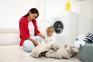 Photo of Smiling housewife with her baby doing laundry at home