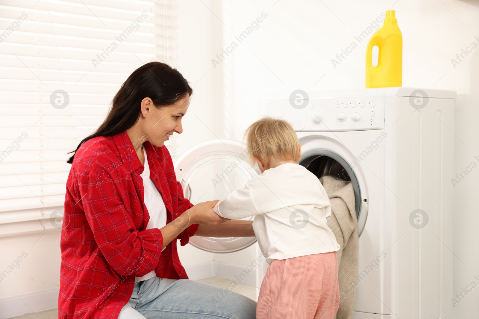 Photo of Smiling housewife with her baby doing laundry at home