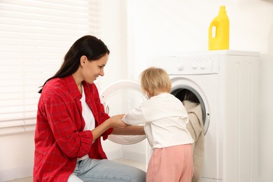 Photo of Smiling housewife with her baby doing laundry at home
