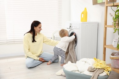 Photo of Smiling housewife with her baby doing laundry at home