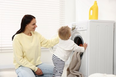 Photo of Smiling housewife with her baby doing laundry at home