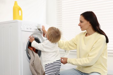 Photo of Smiling housewife with her baby doing laundry at home
