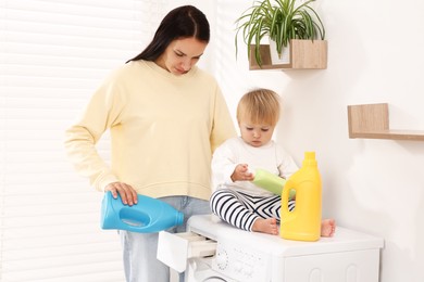 Photo of Housewife and her baby with detergents doing laundry on washing machine near white wall at home