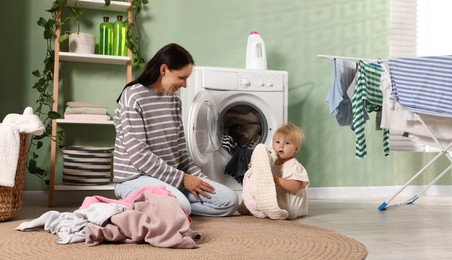 Photo of Smiling mother with her little daughter doing laundry at home