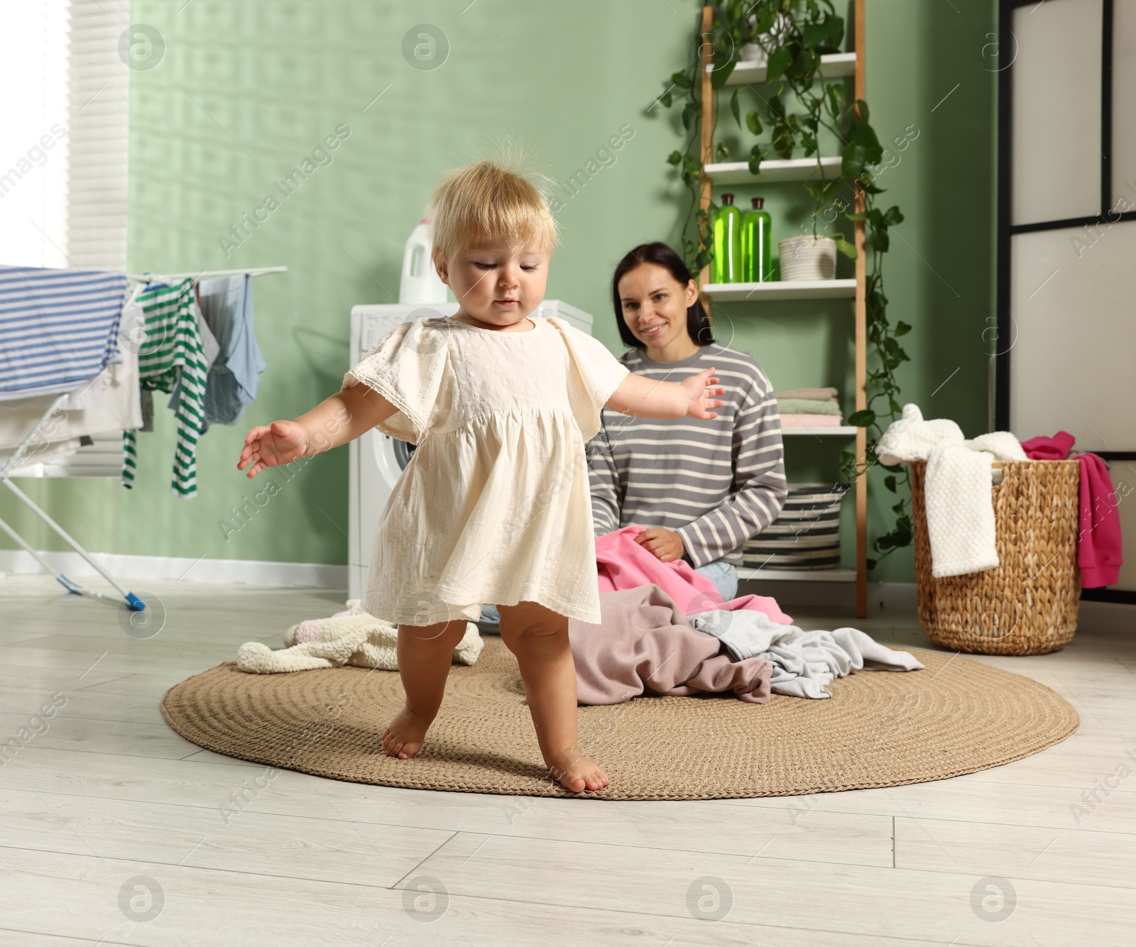Photo of Smiling mother and her little daughter doing laundry at home