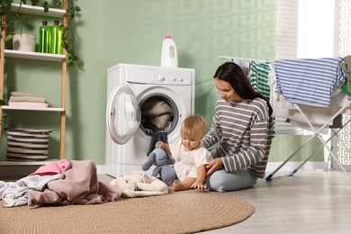 Photo of Smiling mother with her little daughter doing laundry at home