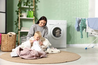 Photo of Smiling mother with her little daughter doing laundry at home