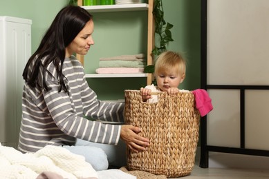 Photo of Mother with her little daughter doing laundry at home