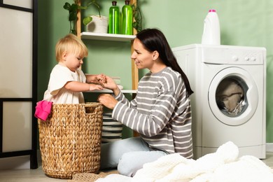 Photo of Smiling mother with her little daughter doing laundry at home
