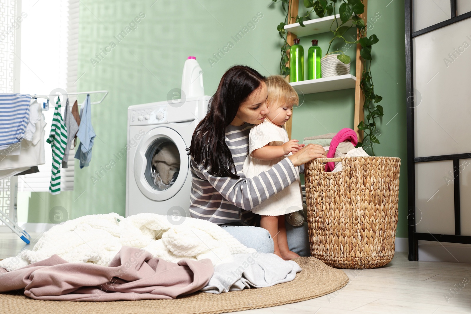 Photo of Mother with her little daughter doing laundry at home