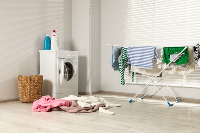 Photo of Washing machine with open door, detergent, drying rack and laundry indoors