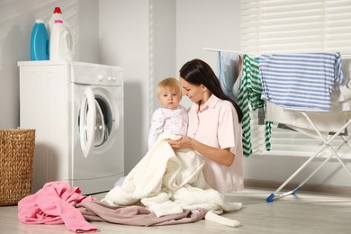 Photo of Smiling mother with her little daughter doing laundry at home