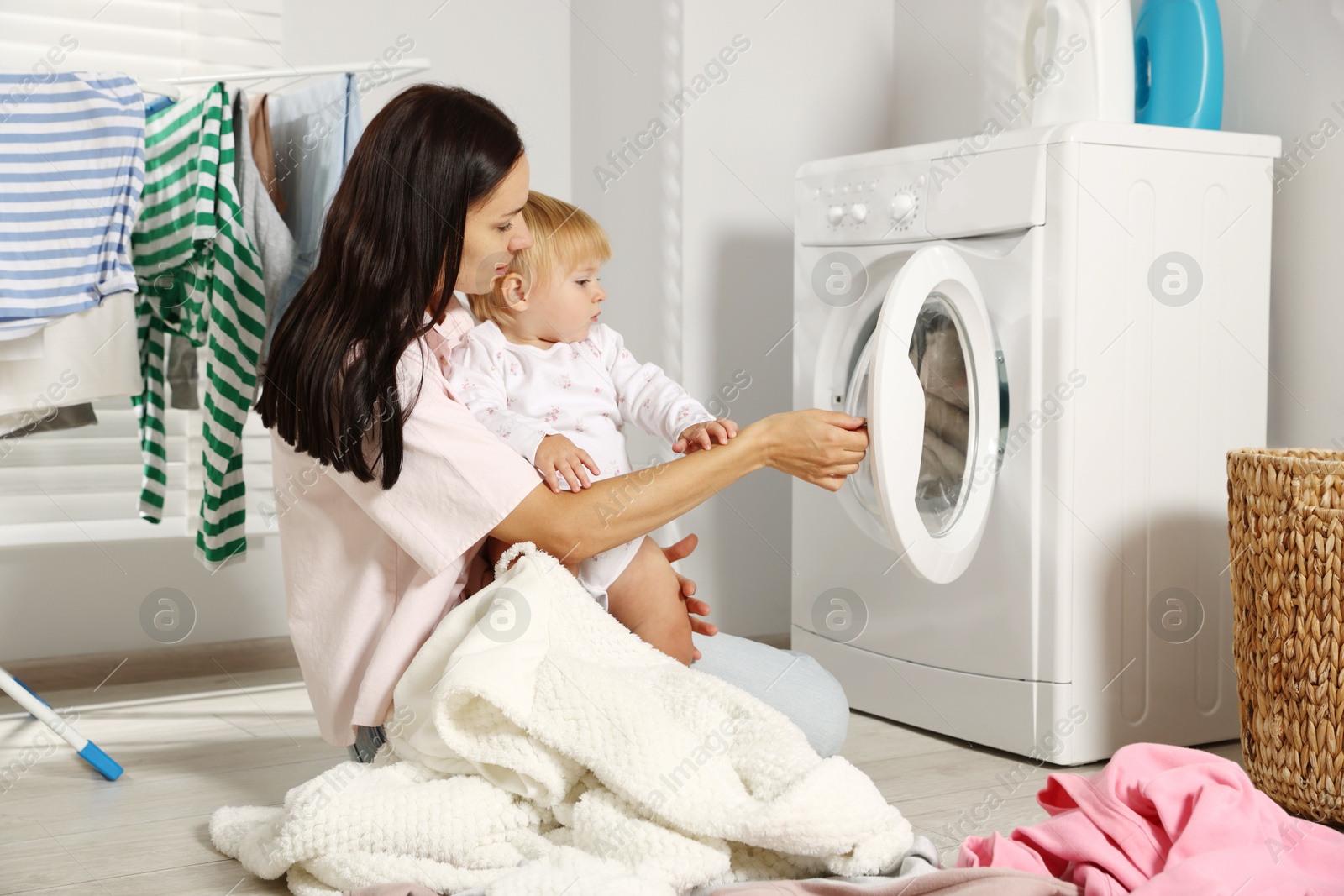 Photo of Mother with her little daughter doing laundry at home