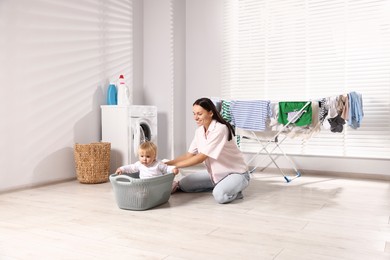 Photo of Smiling mother with her little daughter having fun while doing laundry at home