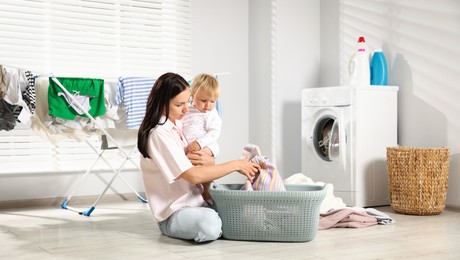 Photo of Mother with her little daughter doing laundry at home