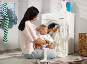 Photo of Smiling mother with her little daughter doing laundry at home