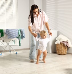 Photo of Smiling mother supporting her daughter while she learning to walk at home