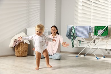 Photo of Smiling mother calling her daughter while she learning to walk at home