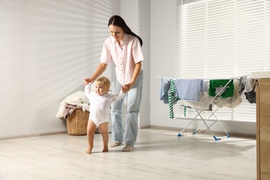 Photo of Smiling mother supporting her daughter while she learning to walk at home