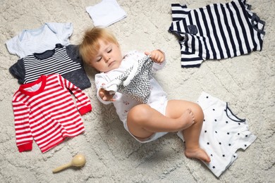 Photo of Cute baby among clean clothes on light carpet, top view