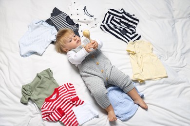 Photo of Cute baby among clean clothes on white bed linens, above view