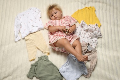 Photo of Cute baby among clean clothes on bed linens, above view