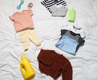 Photo of Different baby clothes, toys and detergents on white bed linens, above view