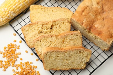 Photo of Freshly baked cut cornbread, seeds and cob on white table, flat lay