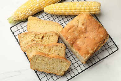 Photo of Freshly baked cut cornbread and cobs on white marble table, top view