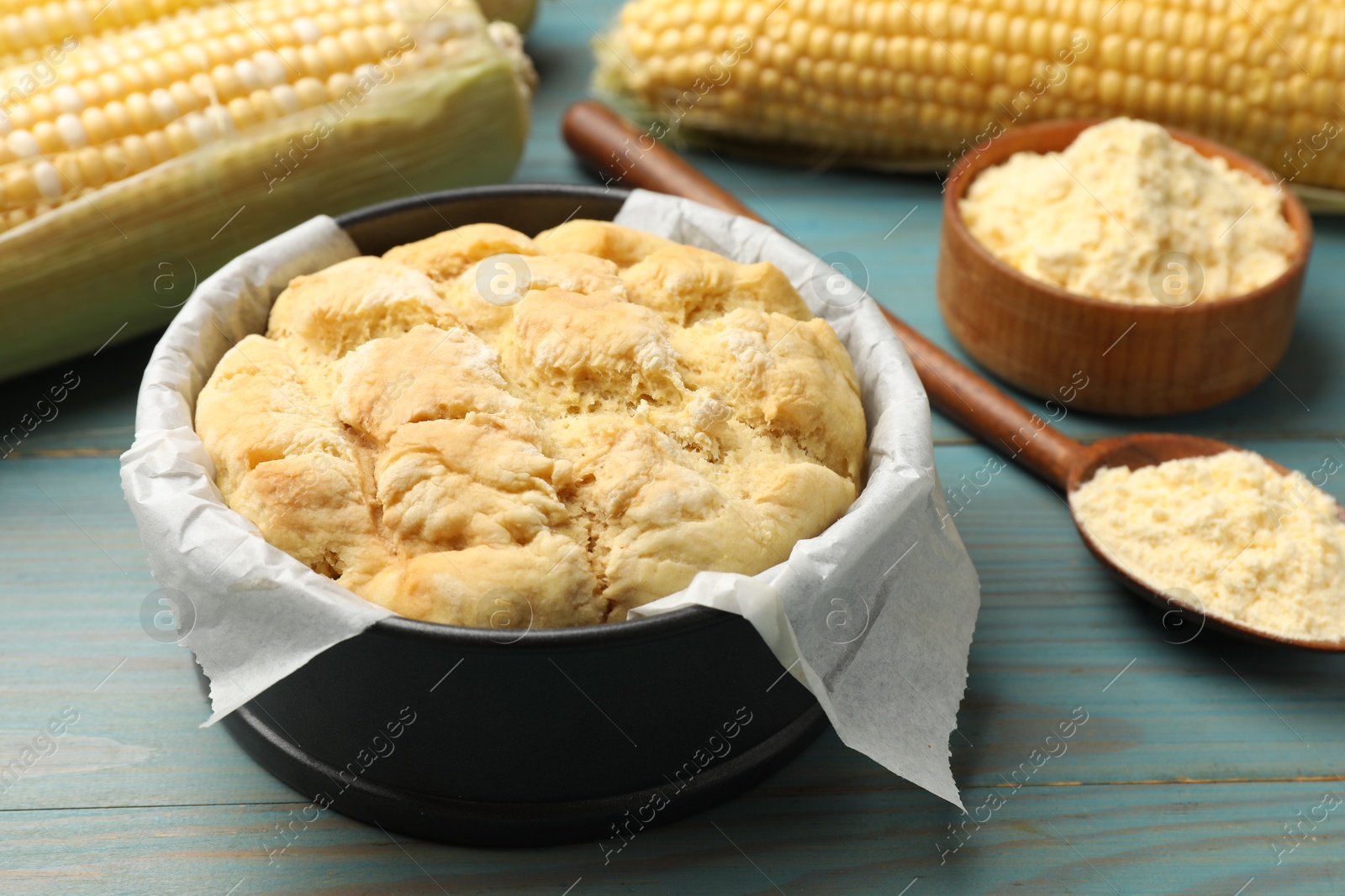 Photo of Freshly baked cornbread, flour and cobs on light blue wooden table, closeup