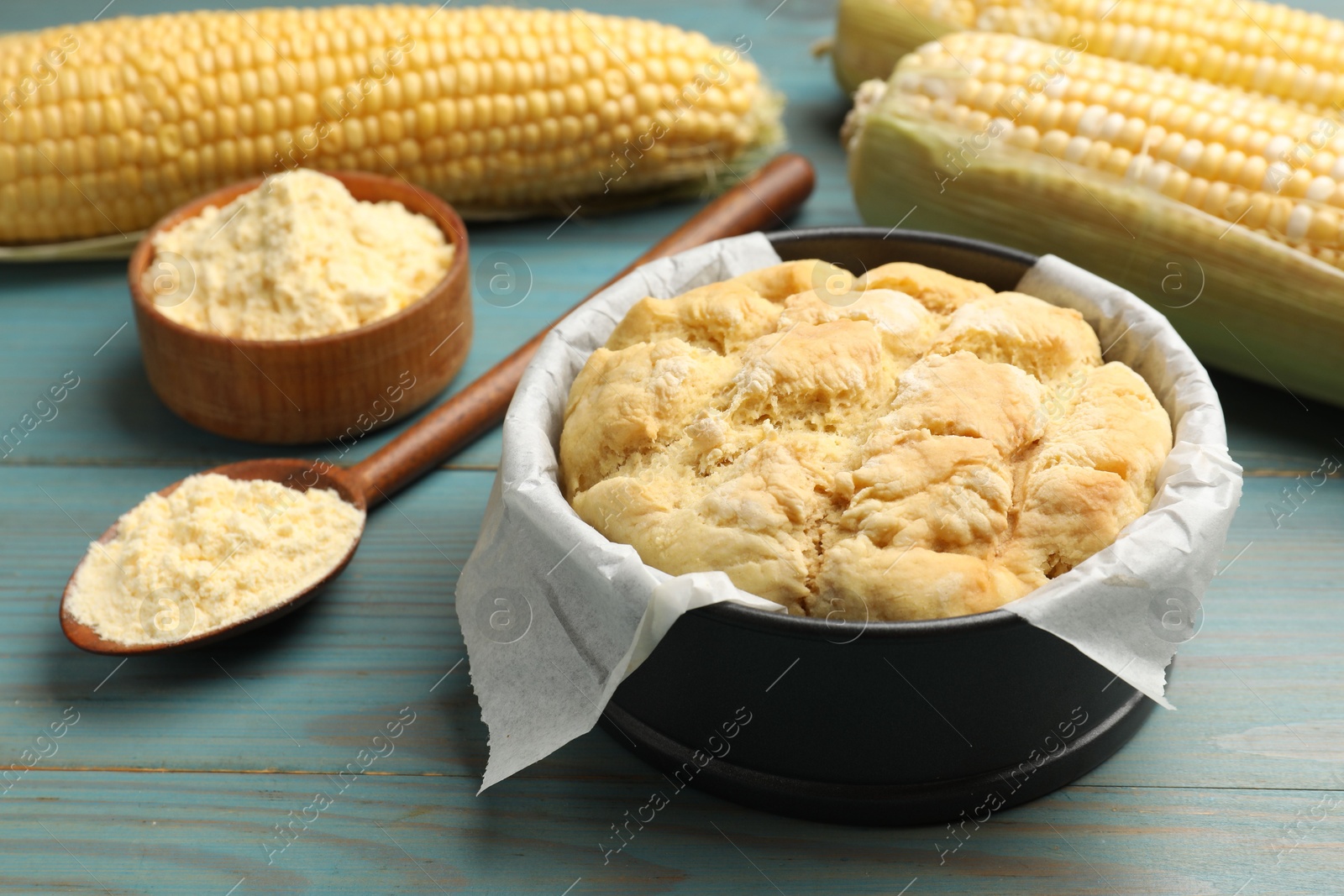 Photo of Freshly baked cornbread, flour and cobs on light blue wooden table, closeup