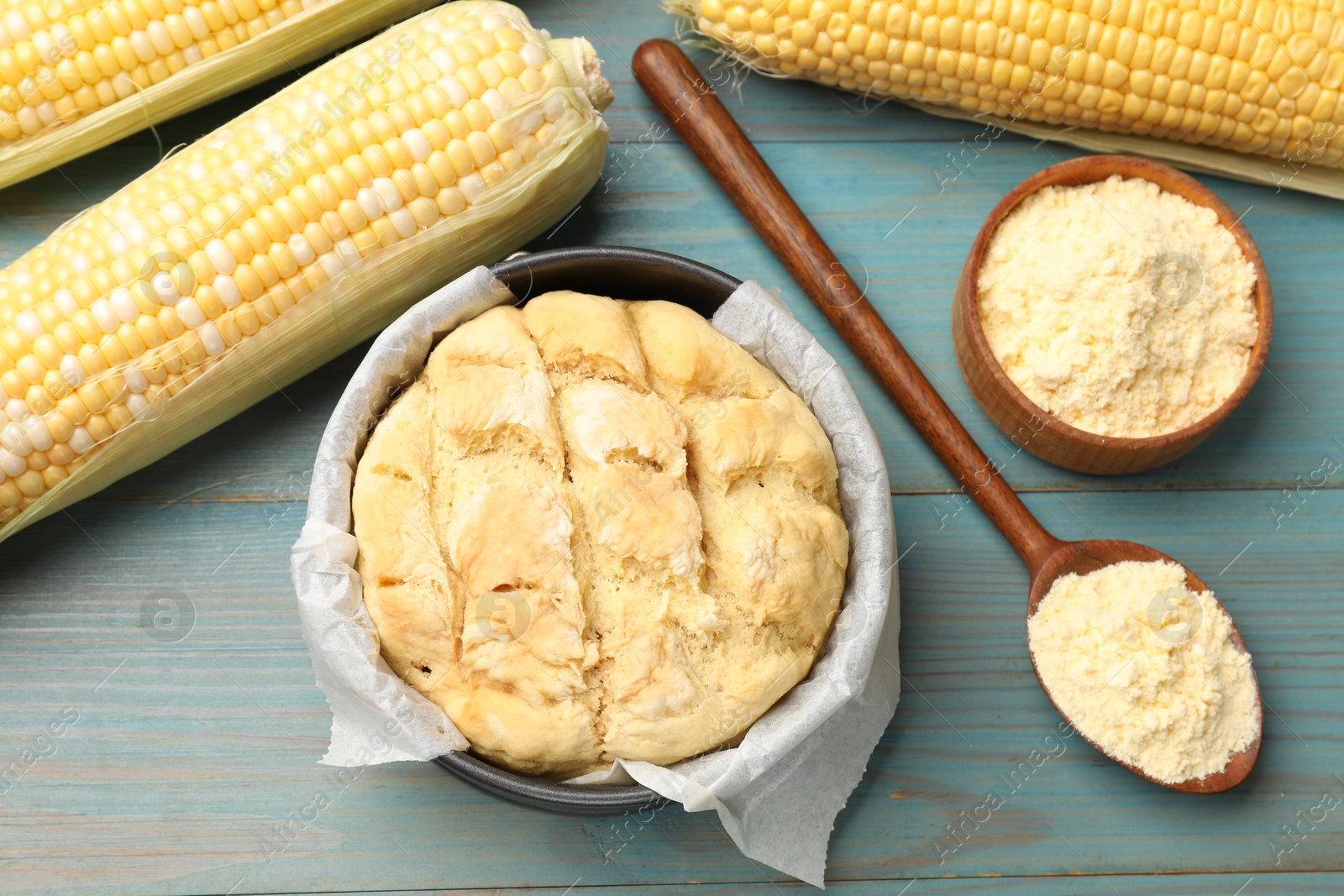 Photo of Freshly baked cornbread, flour and cobs on light blue wooden table, flat lay