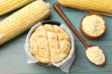 Photo of Freshly baked cornbread, flour and cobs on light blue wooden table, flat lay