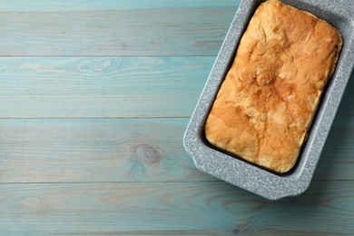 Photo of Freshly baked cornbread in baking dish on light blue wooden table, top view. Space for text