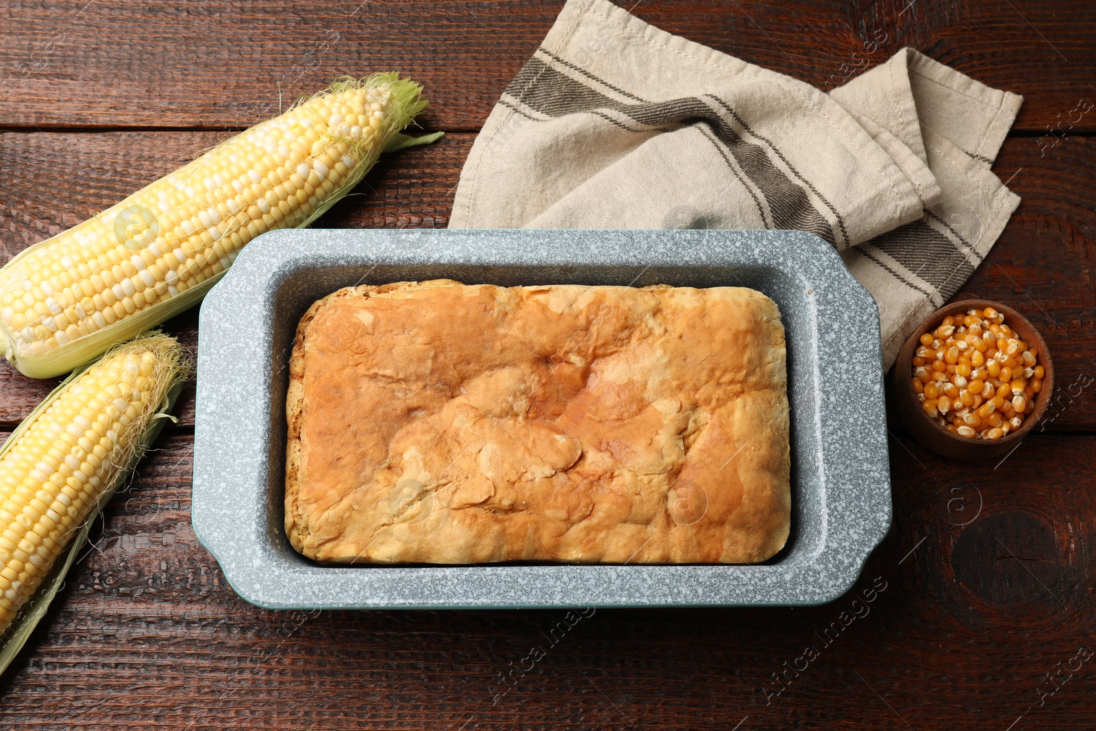 Photo of Freshly baked cornbread, seeds and cobs on wooden table, flat lay