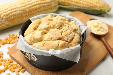 Photo of Freshly baked cornbread, seeds, flour and cobs on white table, closeup