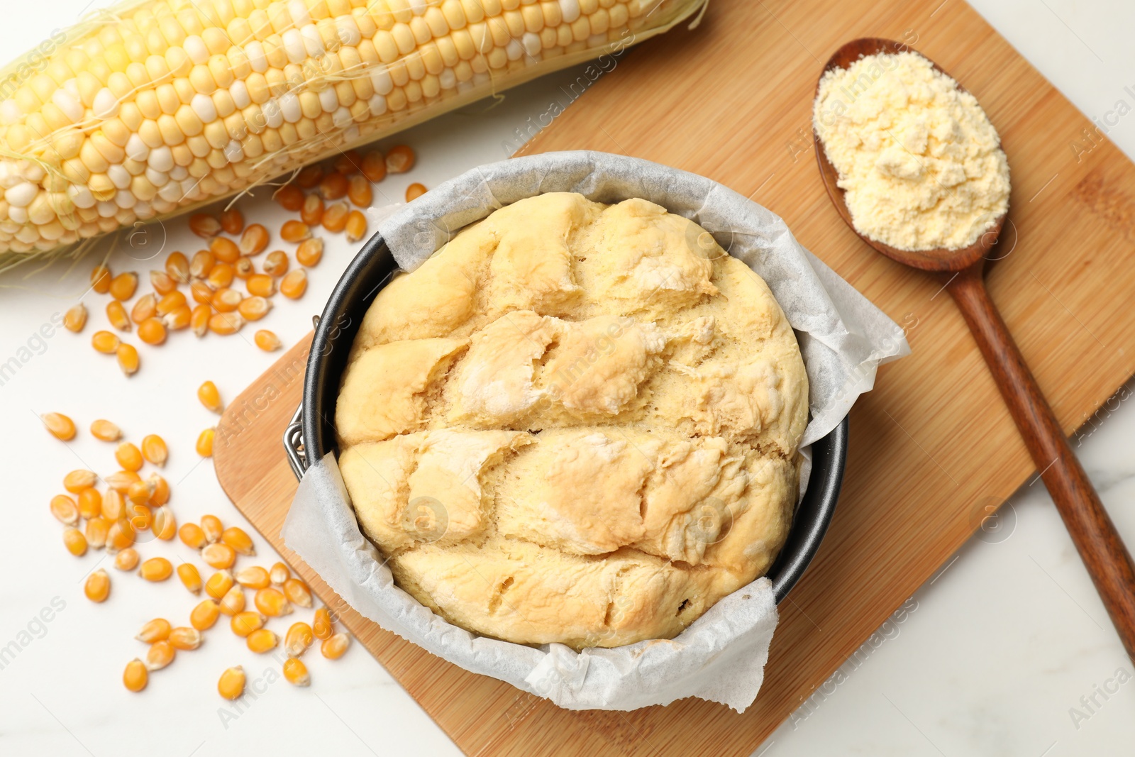 Photo of Freshly baked cornbread, seeds, flour and cob on white marble table, flat lay