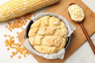 Photo of Freshly baked cornbread, seeds, flour and cob on white marble table, flat lay