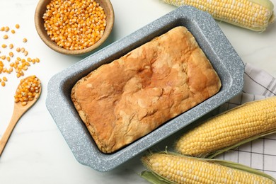 Photo of Freshly baked cornbread, seeds and cobs on white marble table, flat lay